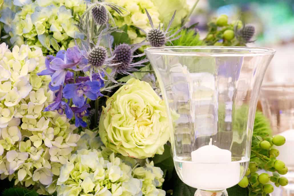 blue and pale green wedding centerpiece with hydrangea, blue sea holly, and roses next to candle hurricane, Dahlia's Florist, Spring Lake NY wedding photographer.