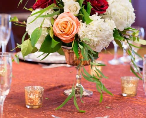 red roses, white roses and hydrangeas and peach roses in mercury glass vase, wedding table centerpiece, burnt orange crushed silk tablecloth, mercury class tea light holders, silver chargers, Kristin Rockhill florist, Nassau Inn, Princeton NJ wedding photographer.