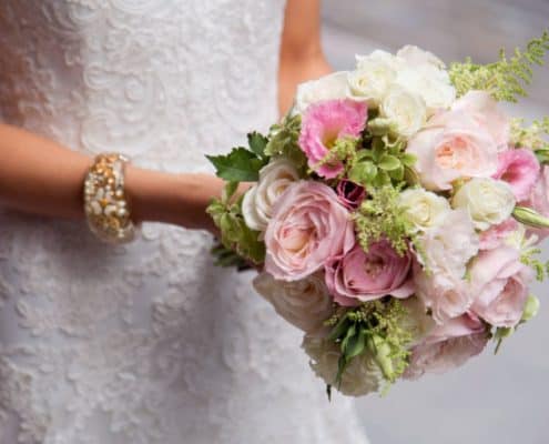 pink and white rose and peony bridal bouquet with green accents held out by bride, white and gold bracelet, Etsuko Planning, River cafe brookly NY wedding photographer.