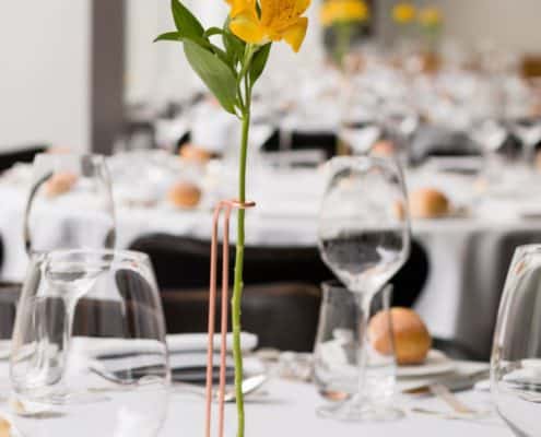 Single stem flower stand, copper arm, white base, yellow flower, white table linens, clear stemware, Karen Brown Events NYC wedding photographer.