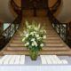 White and green floral arrangement in center of name card table at bottom of grand staircase at Jasna Polana, Princeton NJ wedding photographer, Janet Makrancy's Weddings and Parties Florist.