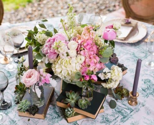 vintage inspired wedding table centerpiece. Hydrangea and pink peony floral arrangements surrounded by bud vases and succulents stacked on old hard cover books. vintage tablecloth, gold chargers, gold flatware, Kristin Rockhill florist, Chauncey Center Princeton NJ wedding photographer