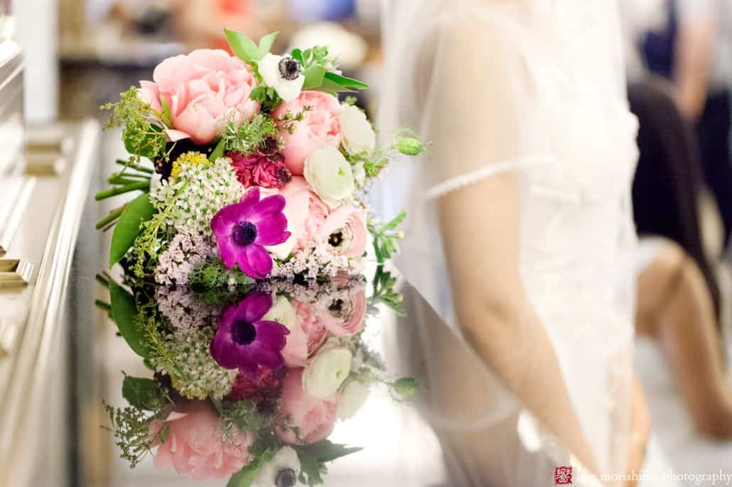 Pink, fuschia and white wedding bouquet lies on reflective surface with bride in background. Homecoming florist. NYC City Hall elopement photographer.