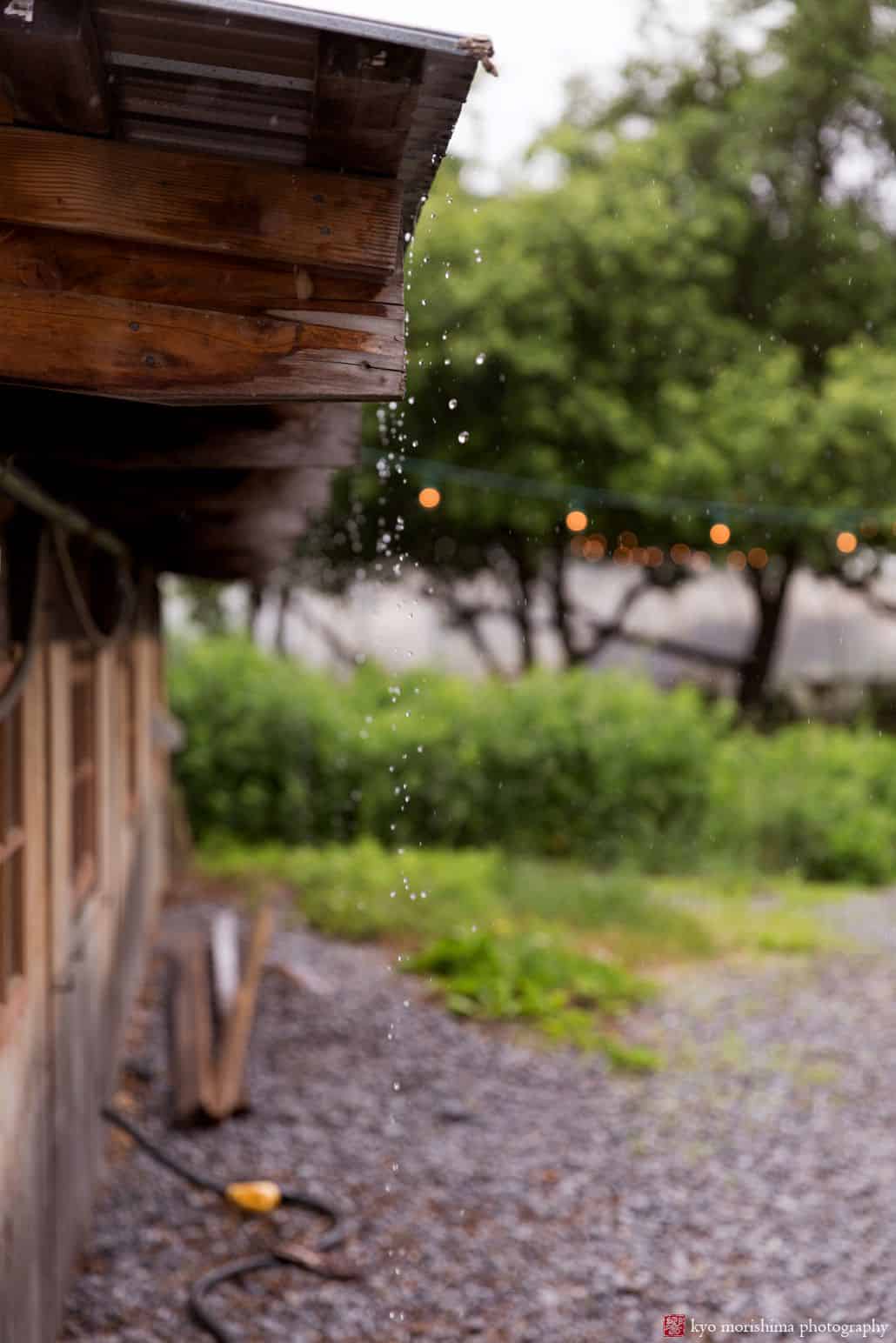 rain drops fall and splash from tin rooftop onto gravel path at Blooming Hill Farm wedding. New York wedding photographer. Rain wedding day photos Village Tea Room Cartwright Tents West Point Tours West Philadelphia Orchestra Hudson Valley Ceremonies Designer Loft Catbird Catherine Angiel 