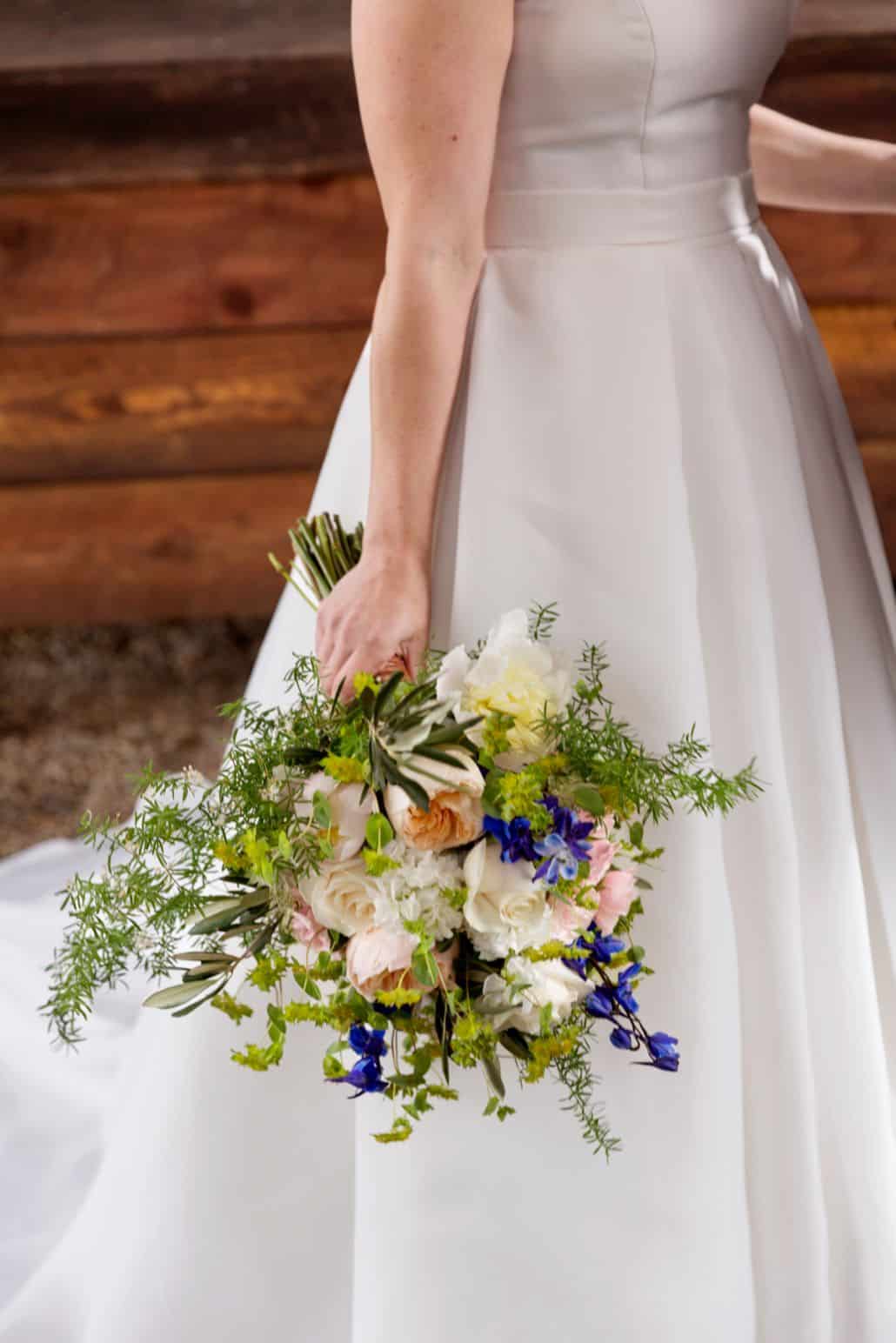 bride holds pink and white bridal bouquet with blue accents at her side at Blooming hill farm in Blooming Grove New York, Fleur di Re florist, New York wedding photographer.