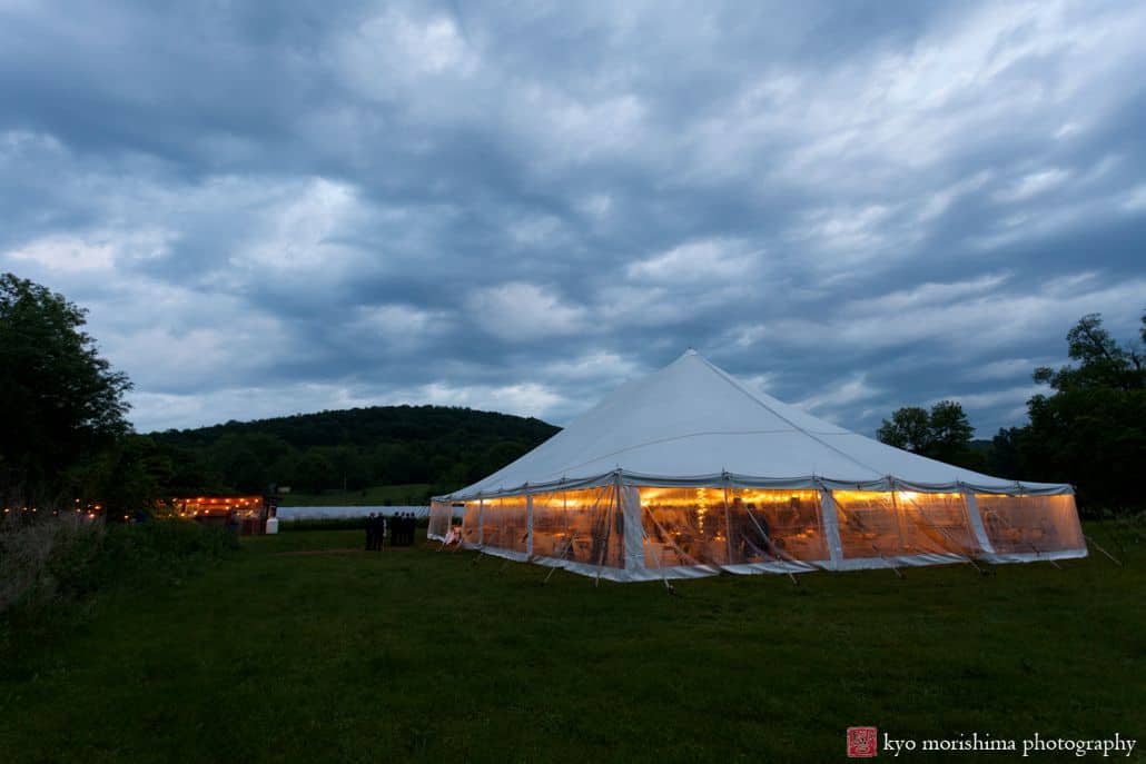 Cartwright wedding tent at dusk and cloudy skies at Blooming Hill Farm wedding. Background hills, foreground grassy turf, NYC Summer rainy day wedding photographer. Hudson Valley Kyo Morishima Photography