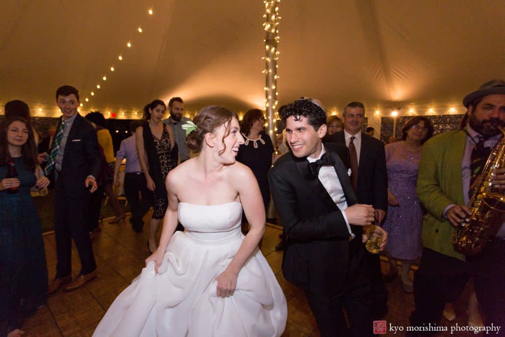 Bride and groom smile at each other and dance enthusiastically at Blooming Hill Farm wedding as west Philadelphia orchestra plays, Cartwright tent, Designer Loft bridal gown, Hudson Valley Ceremonies wedding planner, NYC Jewish wedding photographer. groom wears bow tie and kippah. Kyo Morishima Photography