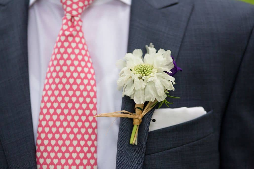 white scabiosa boutineer wrapped with raffia, dark gray suit, white pocket square, red tie with white hearts, Stem cut flowers florist, lake geneva, Wisconsin wedding photographer.