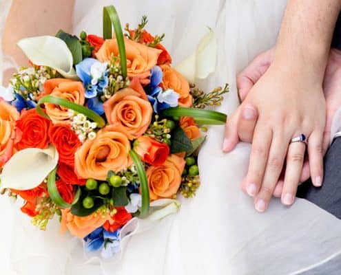 Orange, blue and white wedding bouquet, roses, calla lilies, bride holds bouquet in her lap while holding groom's hand. dark blue gem engagement ring, whole foods florist, cap and gown club, Princeton, NJ wedding photographer.