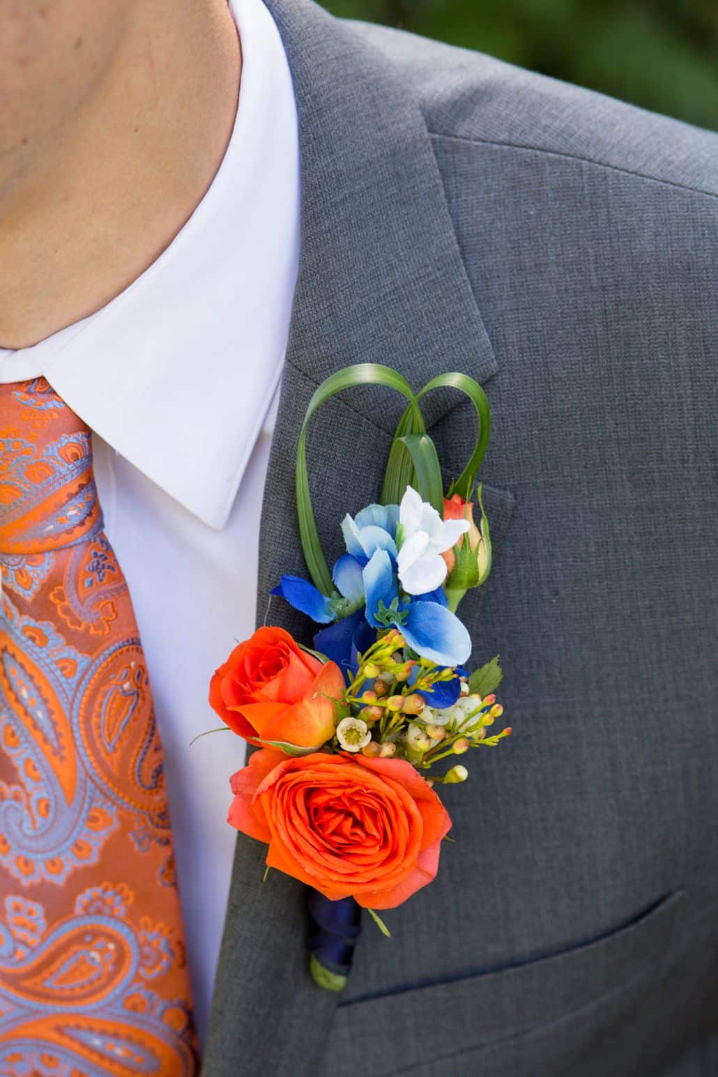 orange and blue boutinneer wrapped with navy ribbon, roses, glossy green grassy accents, groom wears gray suit, blue and orange paisley tie, Whole Foods florist, Cap and Gown Club, Princeton ,NJ wedding photographer.