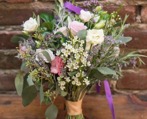 bridal bouquet on wooden ledge in front of old brick wall at Frankie's 457 Spuntino, vintage floral arrangement, white, pink, silvery leaves, purple ribbon, Opalia florist, Brooklyn, NY wedding photographer.