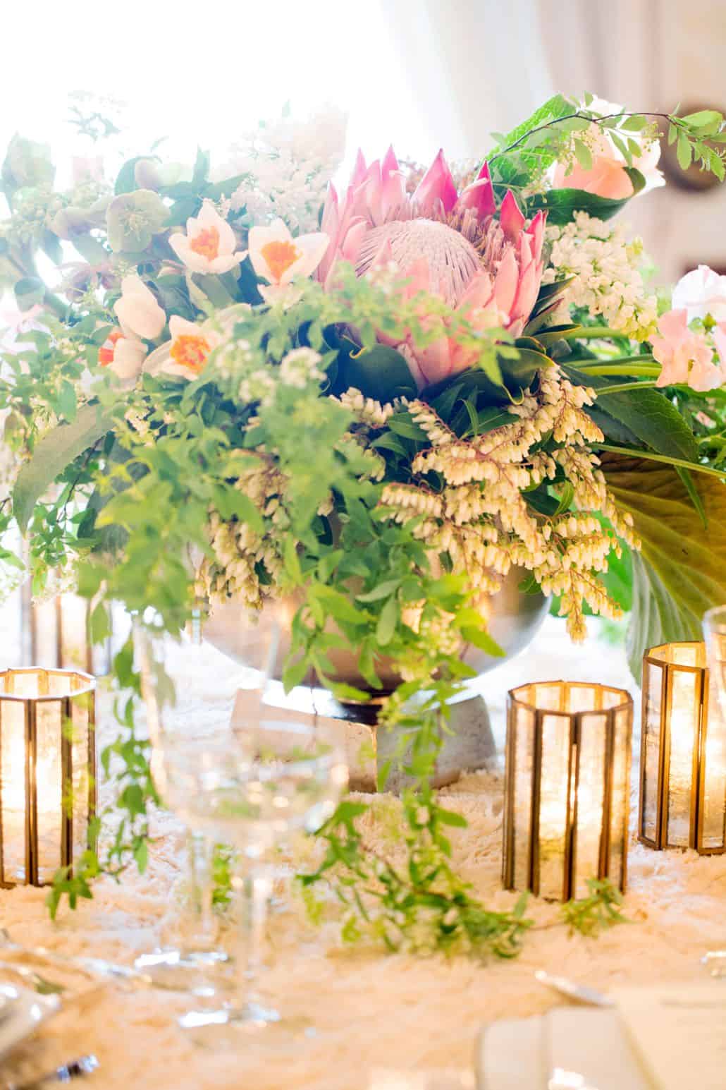 wedding table centerpiece in large silver urn, king protea flowers and hanging leaves, gold candle holders, white lace tablecloth, Viburnum florist, Nassau Inn, Princeton, NJ wedding photographer.