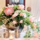 wedding table centerpiece with large gold urn filled with pink and white flowers with trailing leaves, king protea, tulips, gold candle holders, white lace tablecloths, Viburnum florist, Nassau Inn, Princeton, NJ wedding photographer.