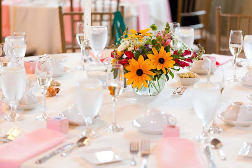 wedding table decor, small round flower arrangement in round, clear glass vase, black eyed susan, snap dragon, yellow, pink, purple, fuscia, white, green, pale pink napkins, white tablecloth, chiavari chairs, Wildflowers of Princeton Junction florist, Mercer Oaks Country Club, Princeton Junction, NJ wedding photographer.