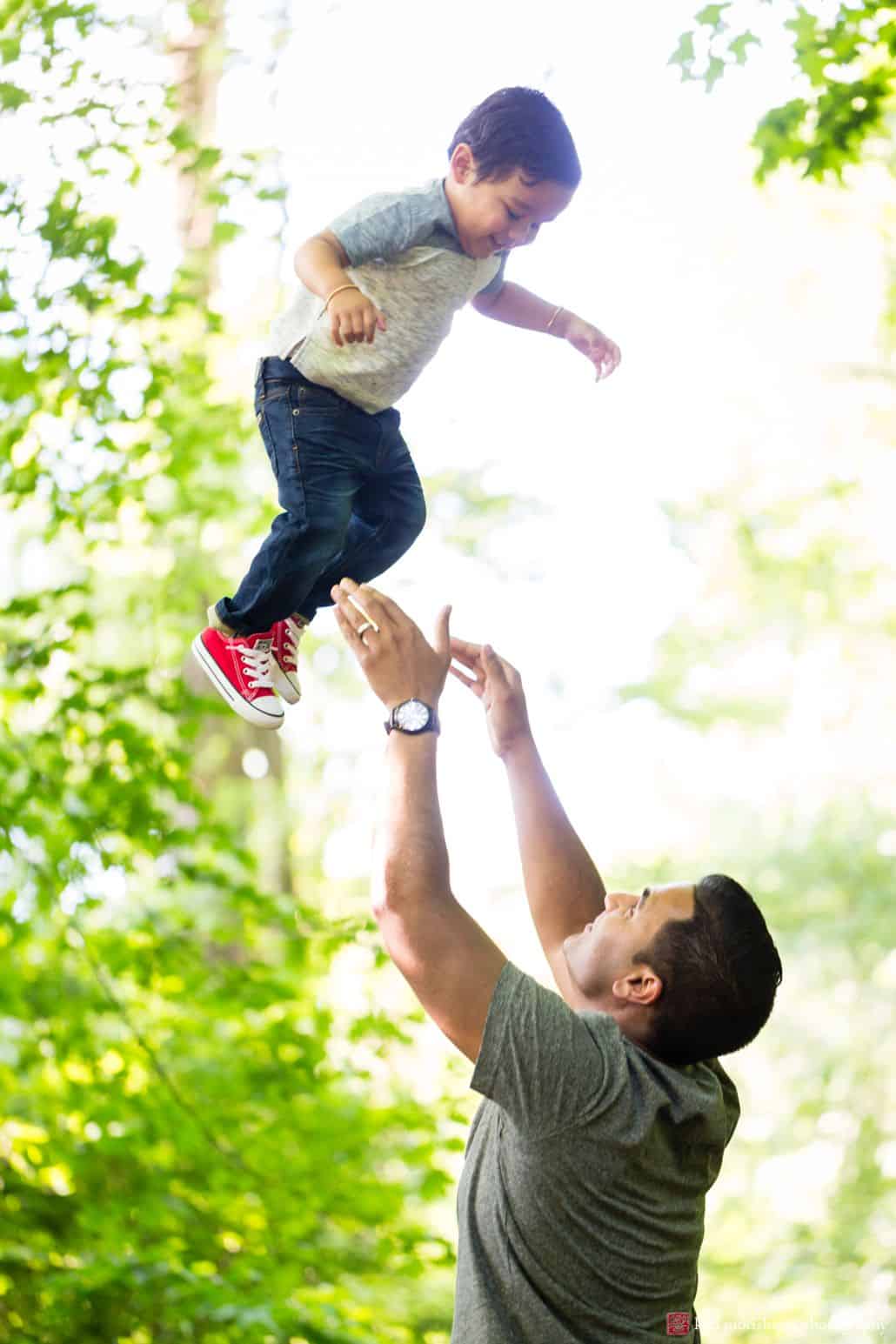 Documentary family photographer: father throws his son into the air during a springtime photo shoot in Princeton