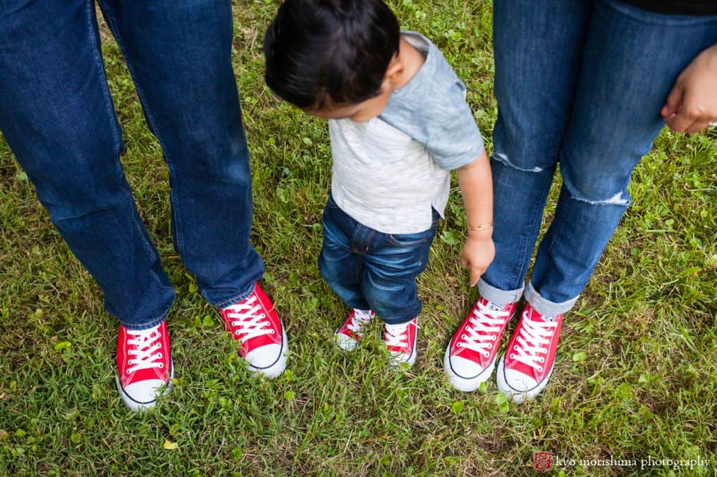 Family photojournalism: little boy looks down at his family's three pairs of red converse sneakers 