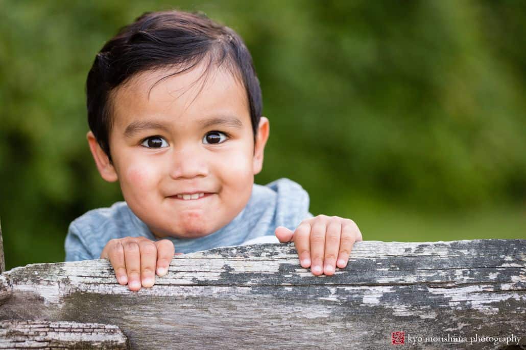 Portrait photographer in Princeton: young boy smiles as he stands on the edge of a wooden fence at Battlefield Park