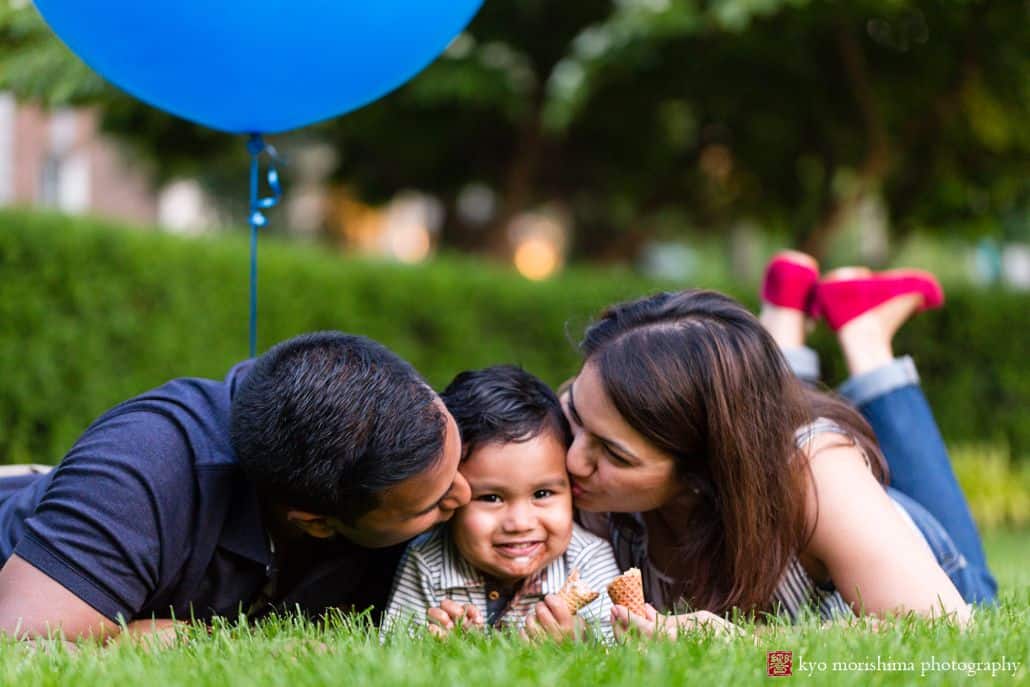 Family photojournalism photography in Princeton: mom and dad give little boy a kiss as they romp around on the grass in Palmer Square