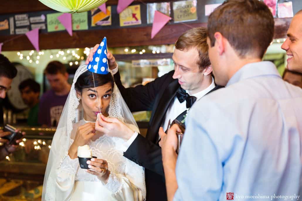 The Bent Spoon wedding portrait: bride eats ice cream while groom adjusts her blue and white polka dot party hat.