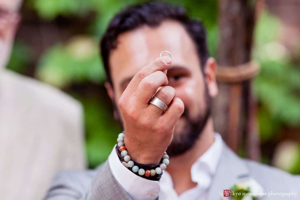 Groom holds up wedding ring by Zoland Jewelry during wedding ceremony at Electric Anvil Tattoo
