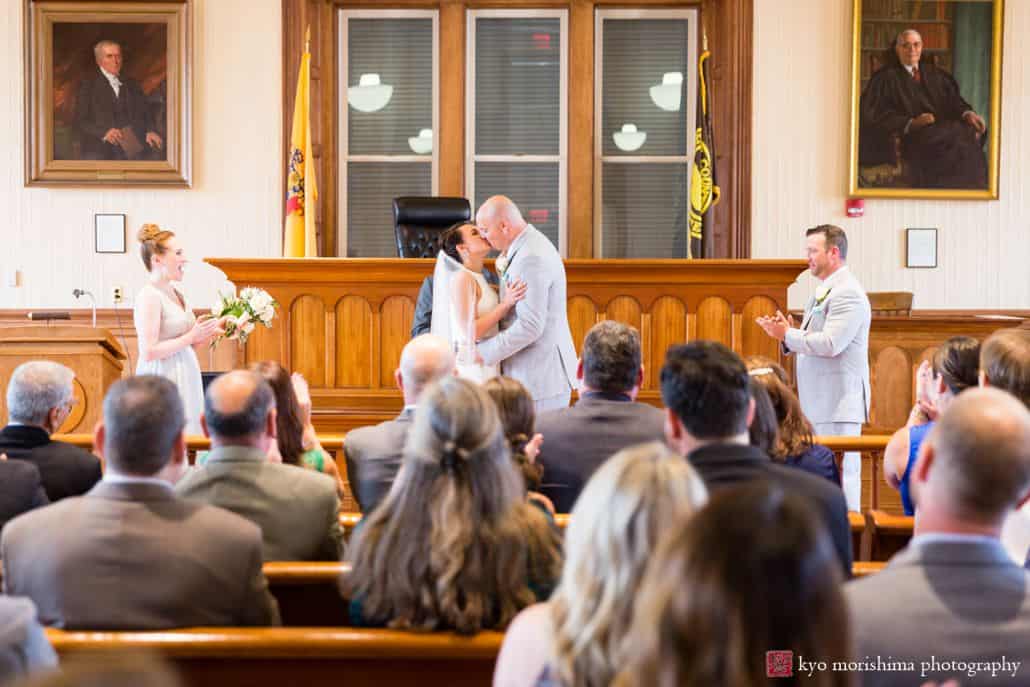 Bride and groom have their first kiss during wedding ceremony as guests applaud at Hunterdon County courthouse, New Hope, PA, BHLDN bridal gown, Men's Warehouse suit, intimate Pennsylvania wedding photographer.