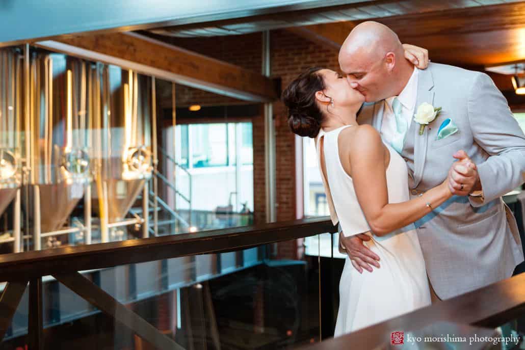 Bride and broom kiss outside bright tanks at Triumph Brewing, BHLDN wedding gown, Men's Warehouse suit, white rose boutineer, The Pod Shope Flowers, New Hope, PA wedding photographer, triumph brewery wedding photos.