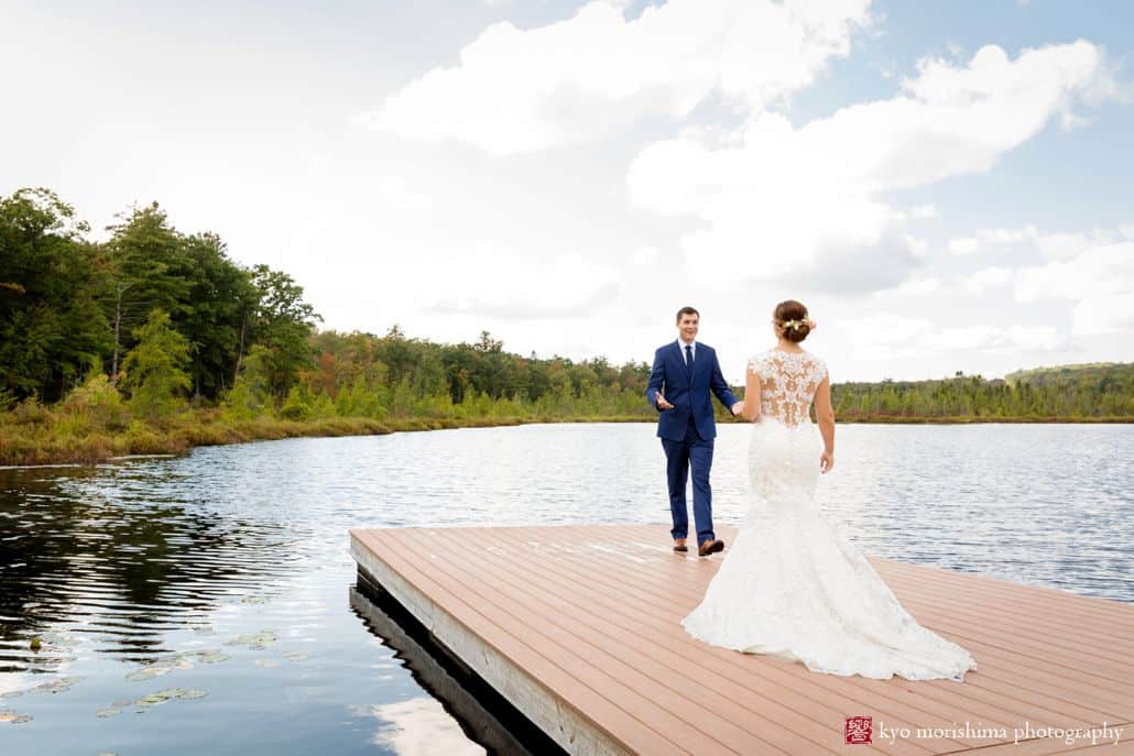 Bride and groom stand at end of dock overlooking a pond and treeline at Woodloch Pines in the Poconos, Castle Couture wedding gown, lace back wedding dress, navy groom's suit, outdoor wedding photographer, resort wedding.