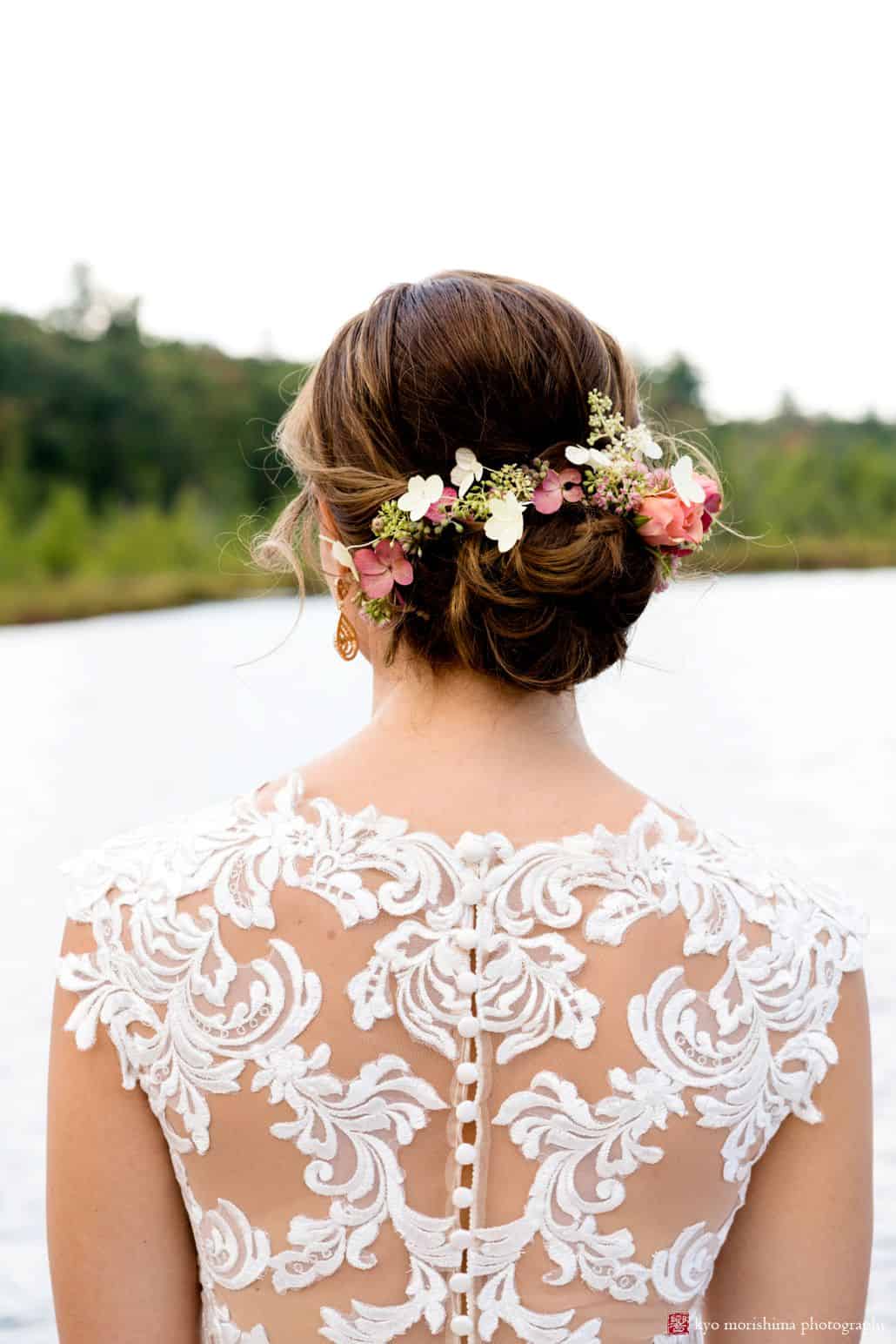 Bride overlooking pond wearing lace back wedding dress by Castle Couture with cloth covered buttons, pink and white flowers in bride's hair with pink rose and eucalyptus seeds, Woodloch Pines wedding photographer, outdoor wedding photography.