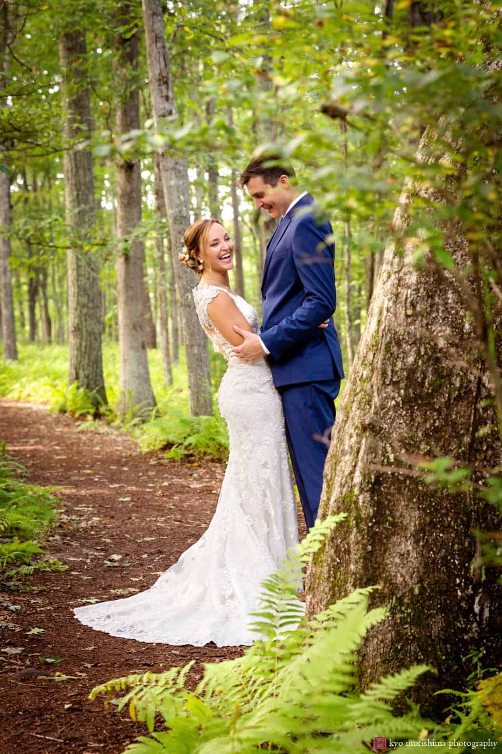 Bride and groom smile on mulched path in wooded area at Woodloch Pines resort, Castle Couture bridal gown, dark blue groom's suit, outdoor wedding photographer.