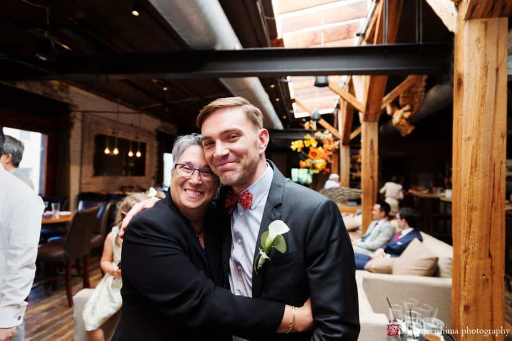 Groom and guest hug and smile for the camera at Virtue Feed and Grain wedding by candid photographer Kyo Morishima