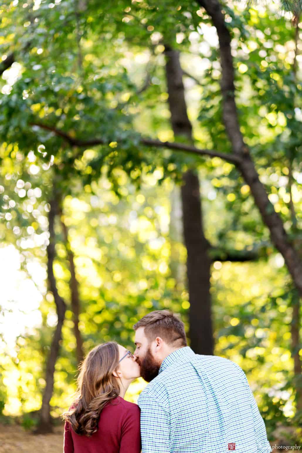 Couple kisses in Prospect Park with bright sunlight filtering through the leaves