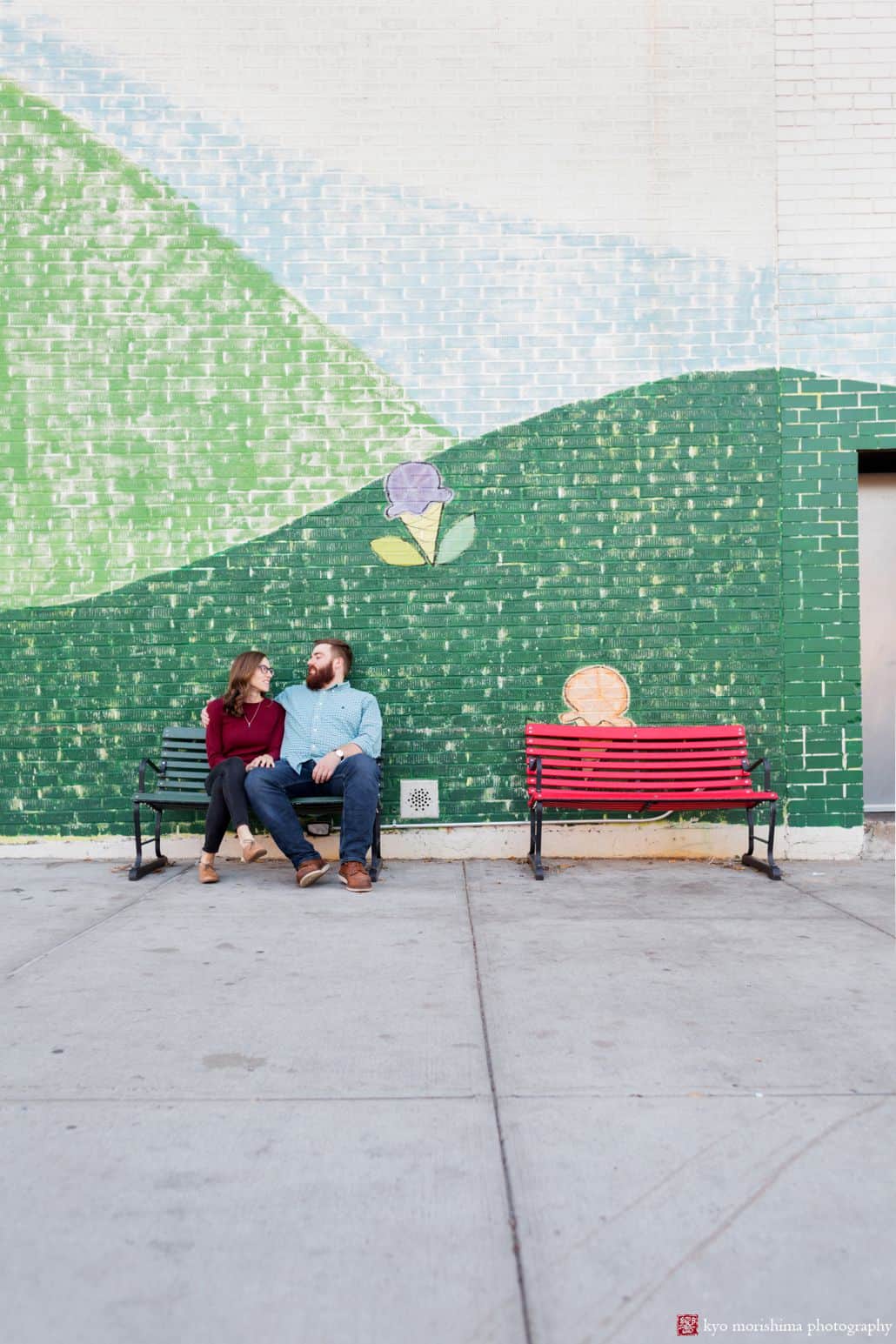 Park Slope engagement photo: couple sits on park bench in front of painted mural