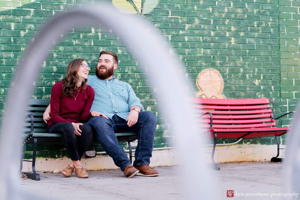 Park Slope engagement photo: couple sits on park bench in front of painted mural