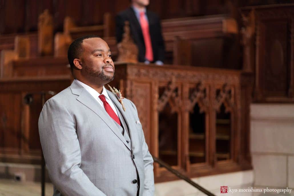 Groom awaits bride at Princeton University chapel wedding, wearing light grey suit with red tie