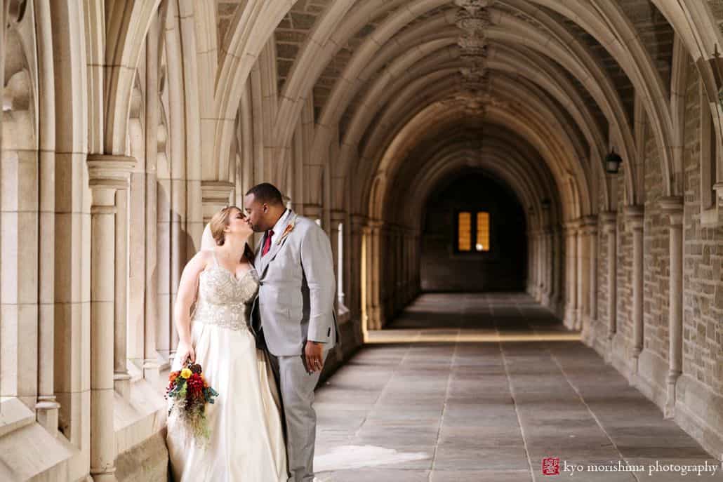 Bride and groom kiss in stone colonnade at Princeton University wedding