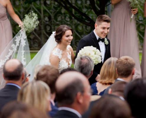 Bride and groom, seen over the tops of their guests' heads, depart the wedding ceremony at Jasna Polana. Bride wears Pronovias. Flowers by Janet Makrancy.