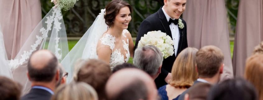 Bride and groom, seen over the tops of their guests' heads, depart the wedding ceremony at Jasna Polana. Bride wears Pronovias. Flowers by Janet Makrancy.