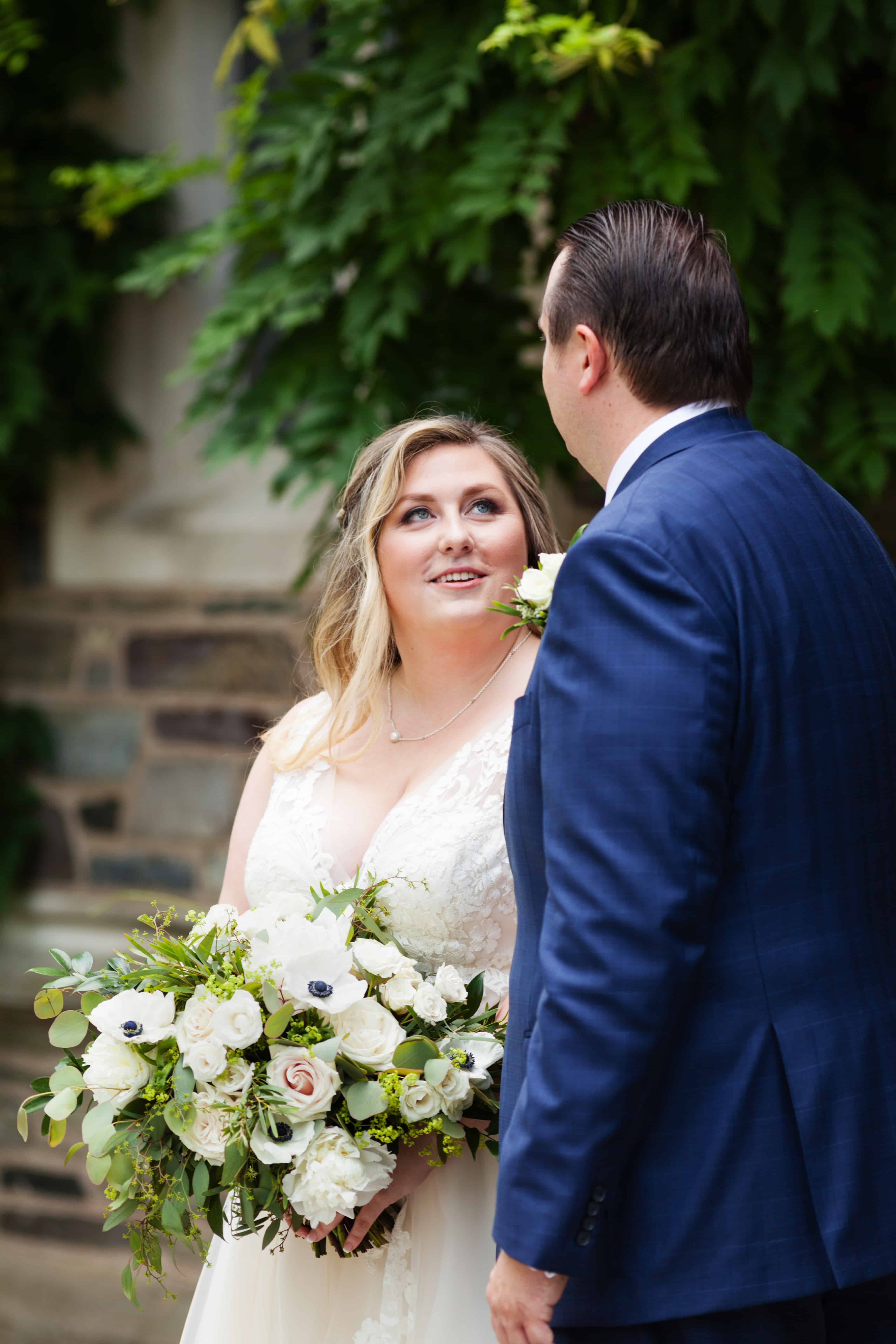 Bride looks up at groom, holding Petal Pushers bouquet, during Princeton University campus wedding portrait session