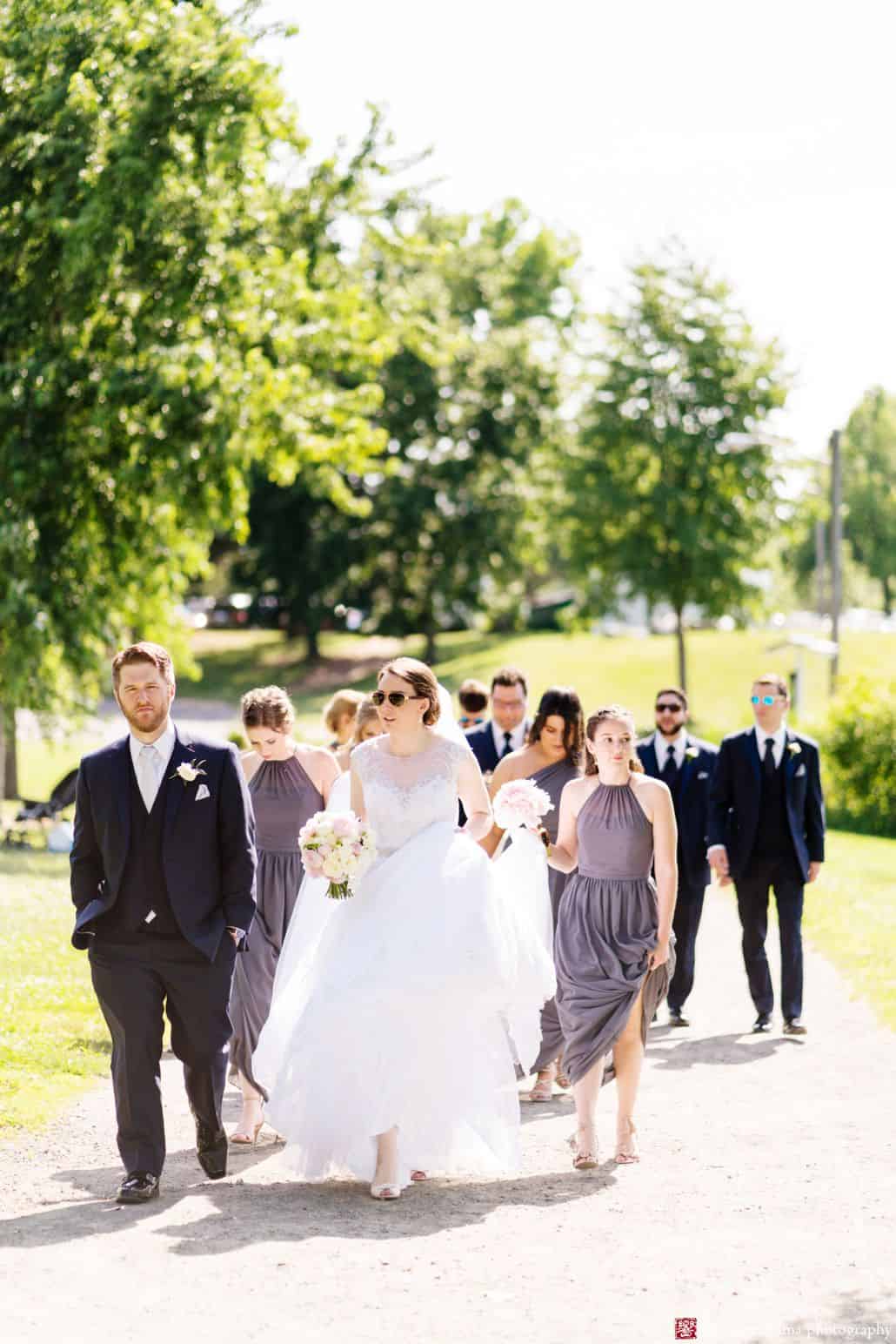 outdoor wedding candid picture bride in wedding dress with groom family walking wearing sunglasses summer wedding by the trees Late Spring Mercer County Boathouse Princeton NJ Wedding