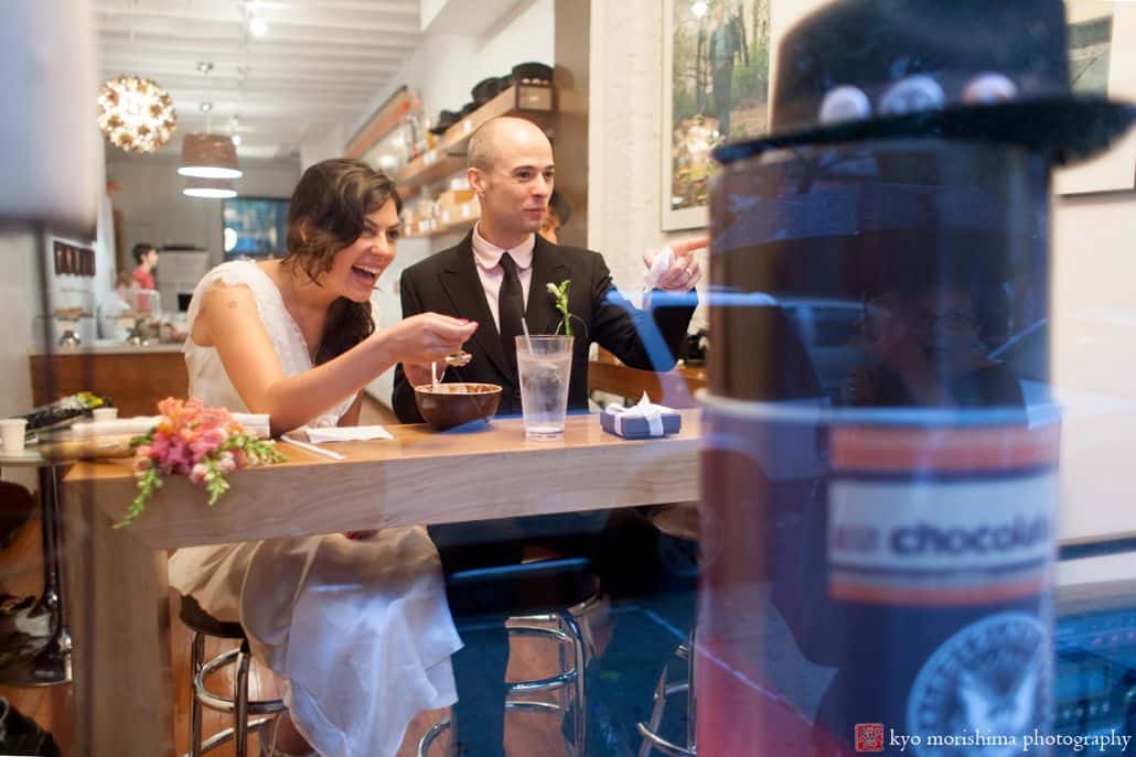 Light-hearted portrait session of a couple seated inside a cafe, happily looking at someone outside the window,the groom is pointing at someone and the bride is smiling as she hold a spoonful of food, photographed by wedding photographer in central NJ Kyo Morishima.