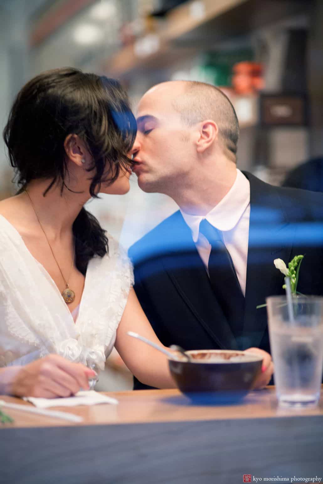 Light-hearted portrait session of a couple who are about to kiss, sitting inside a cafe, and they have a glass of water and a bowl of food on the table, photographed by wedding photographer in central NJ Kyo Morishima.