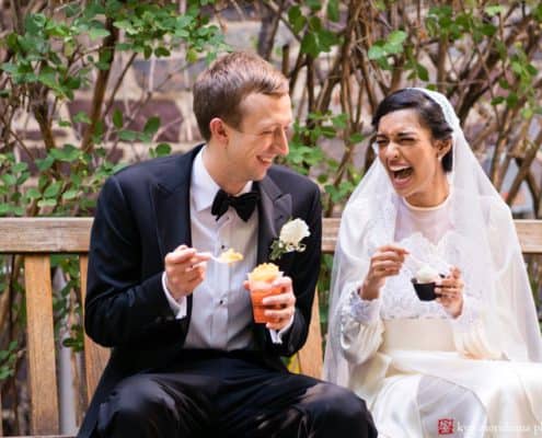 Light-hearted portrait session of a happy groom and bride sitting in a bench, the bride is laughing and holding a cup of ice cream, the groom is smiling holding a glass of ice cream or dessert, photographed by wedding photographer in central NJ Kyo Morishima.