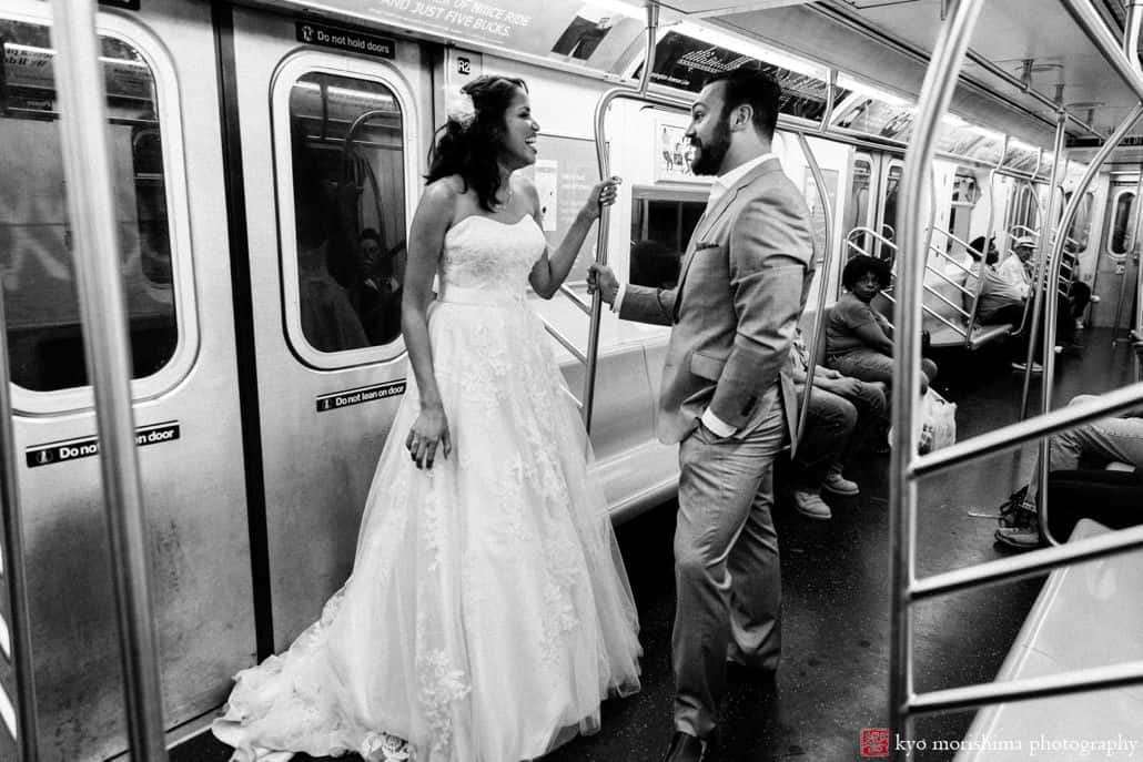 Light-hearted portrait session of a happy groom and bride inside a train, the couple is standing, looking at each other grabbing the train's handles and there are people behind them who are seated, photographed by wedding photographer in central NJ Kyo Morishima.