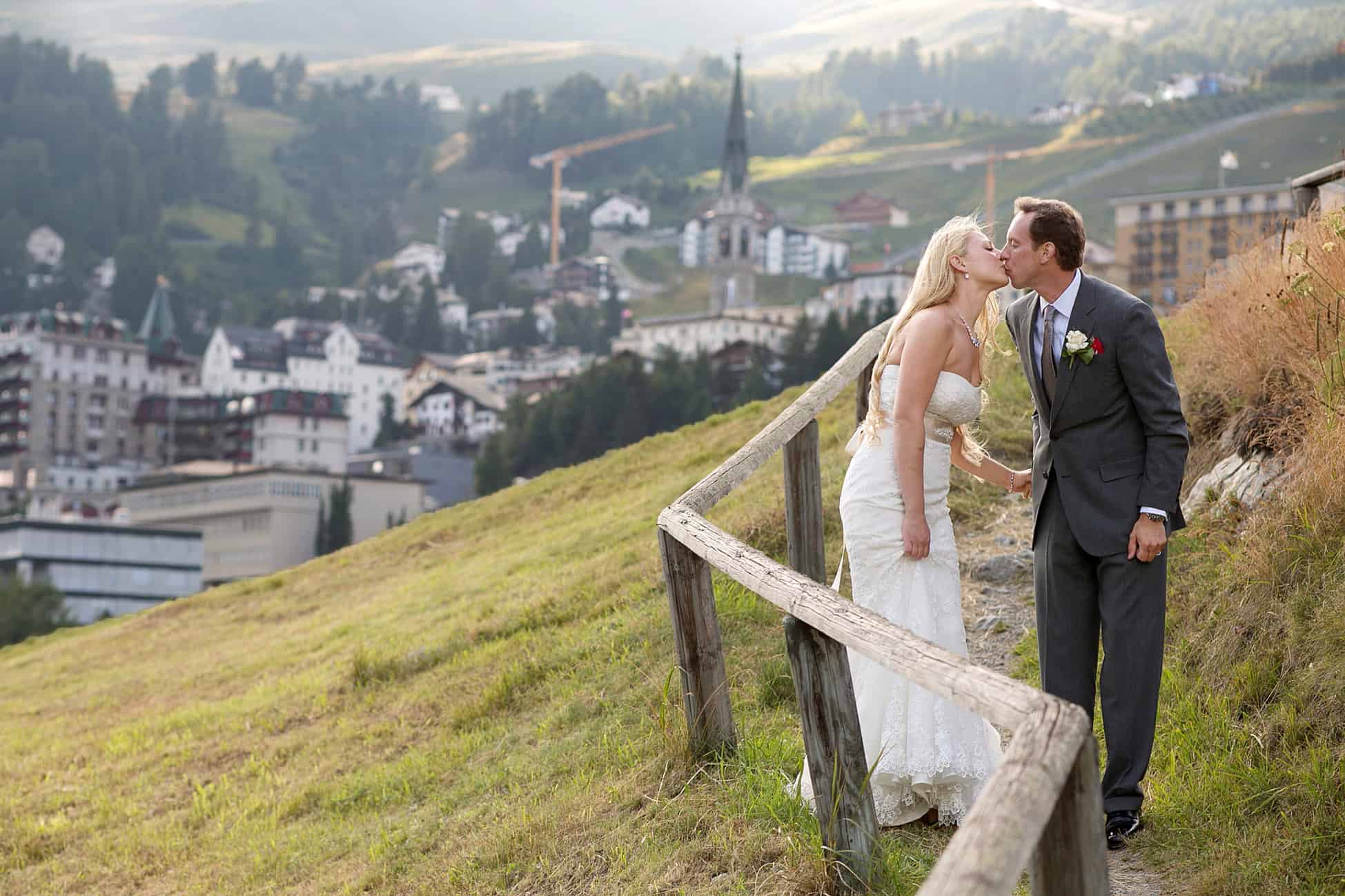 Couple kiss as they walk down gravel path near St. Moritz in the Swiss Alps, photographed by destination wedding photographer in Europe.