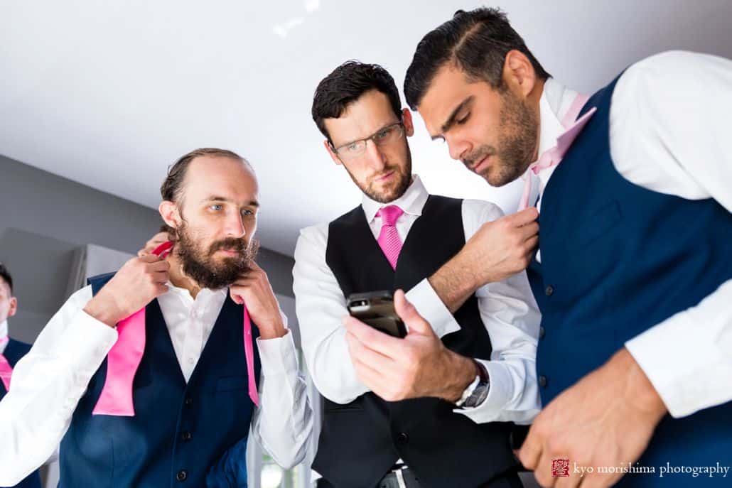 Groom and groomsmen are tying their pink ties while on their phone at a Chauncey Center wedding.