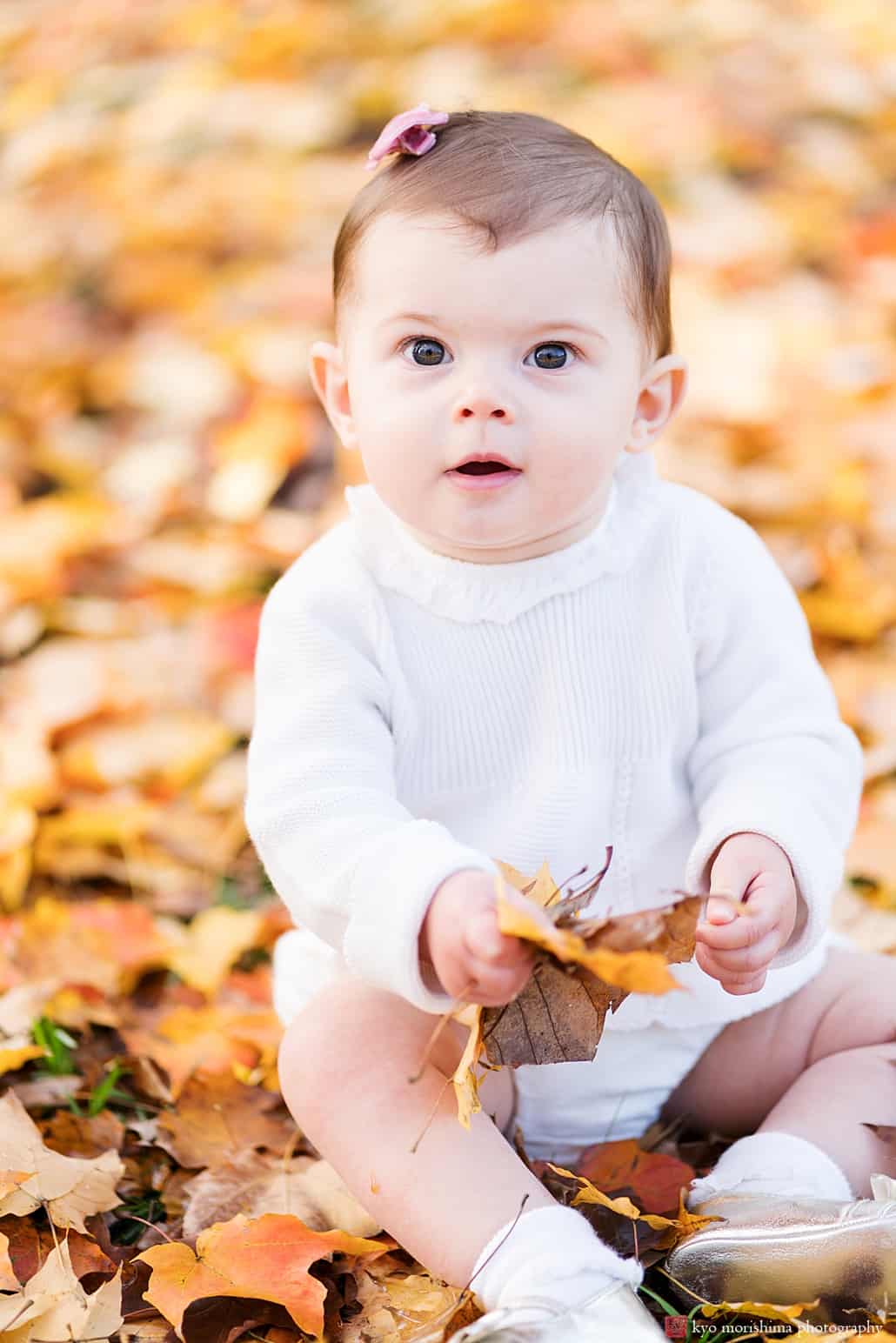 Princeton baby photographer: adorable baby girl wearing white sits outside amidst golden fall leaves