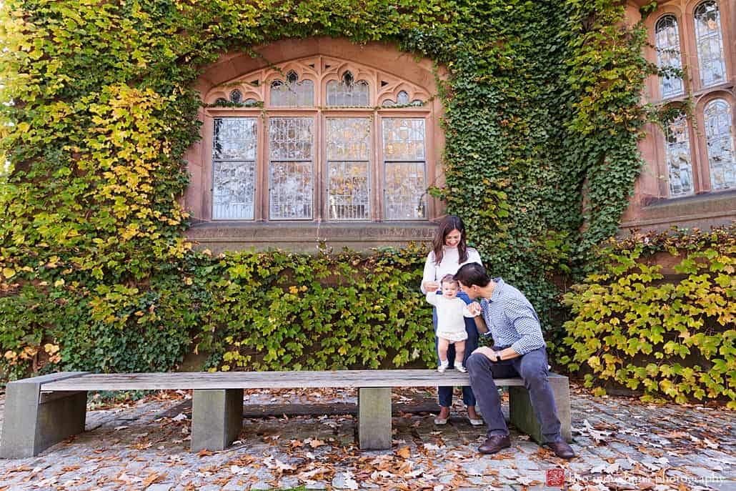 Fun family photographer in Princeton: candid shot on park bench outside ivy-covered wall on Princeton University campus