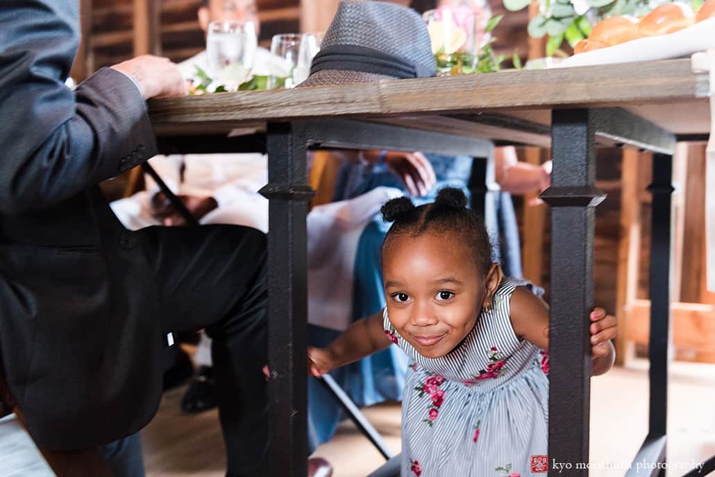 Little girl peeks out from under table during barn wedding reception at Glenmoore Farm in Hopewell NJ