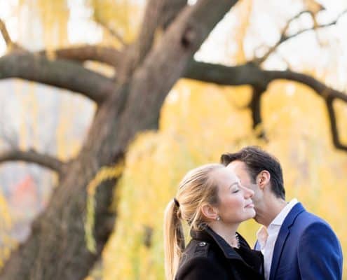 NYC winter engagement photo: kiss with yellow willow tree in the background