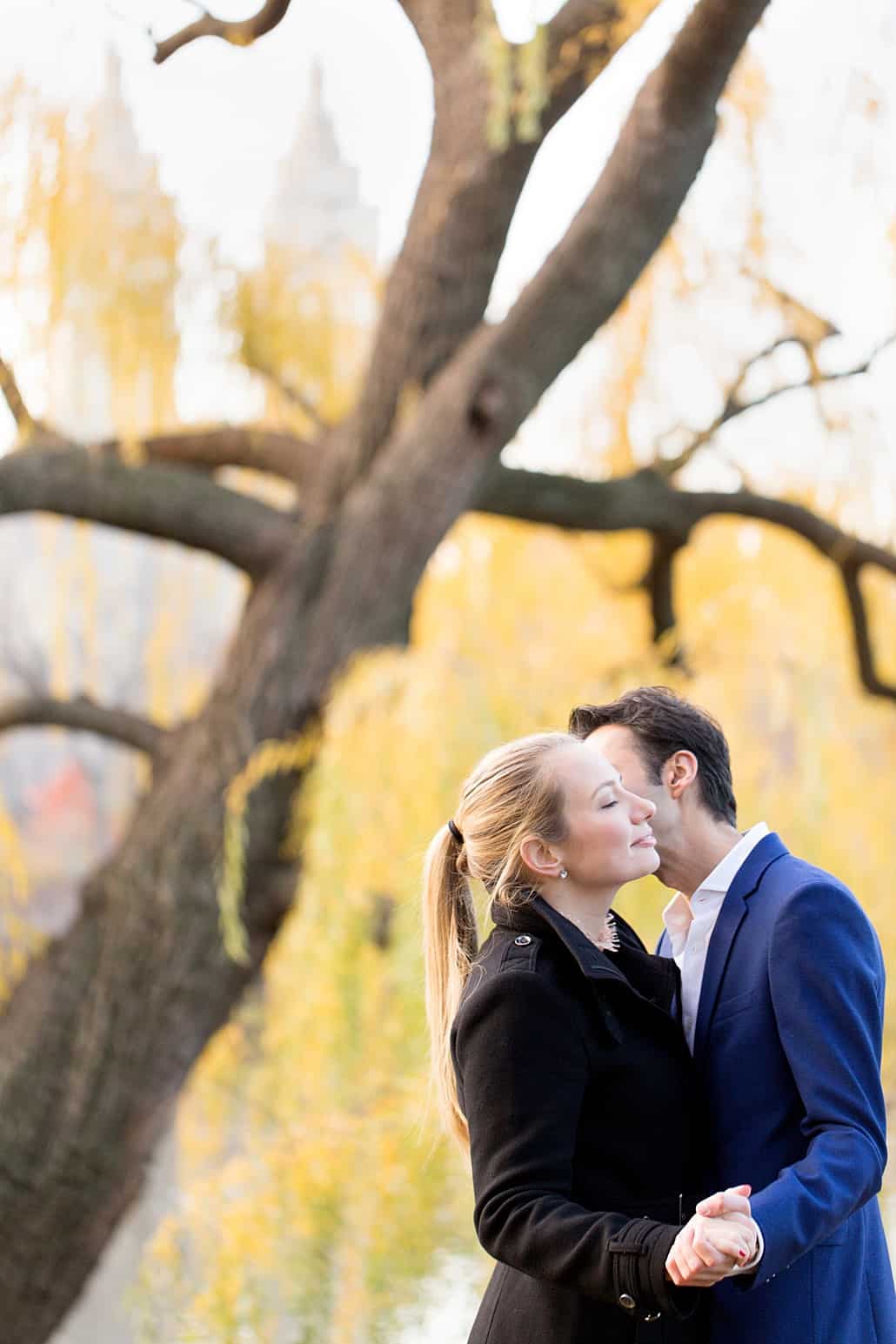 NYC winter engagement photo: kiss with yellow willow tree in the background
